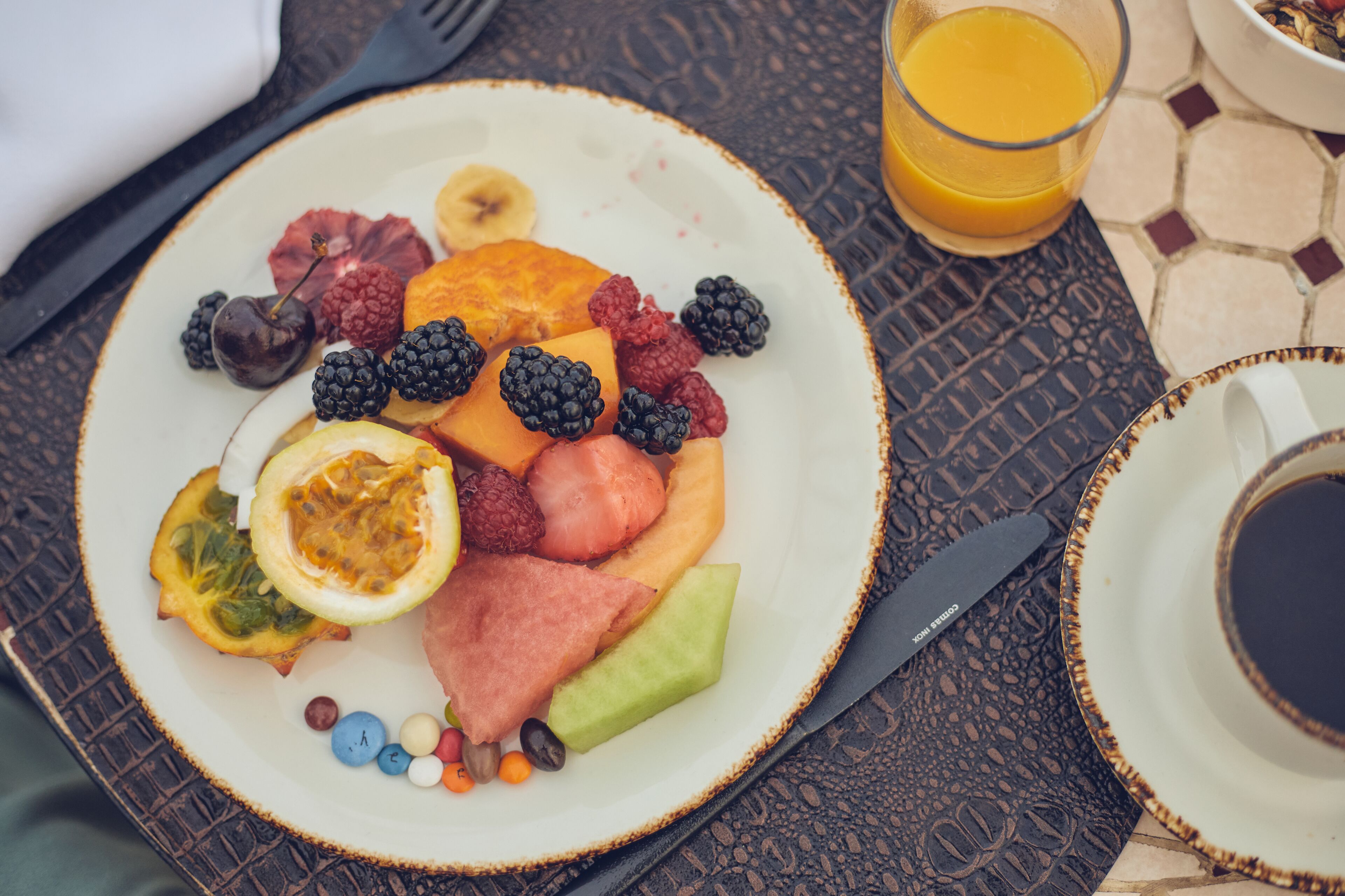 Un plato de desayuno con diversas frutas y un vaso de jugo de naranja sobre una mesa.