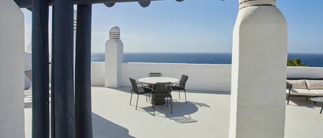 Une terrasse sur le toit avec une table ronde et des chaises, une colonne blanche et une vue sur la mer.