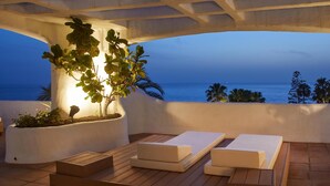 A terrace with wooden lounge chairs and a white planter with plants. - Hyatt Ziva Jardín Tropical Tenerife (Adeje)