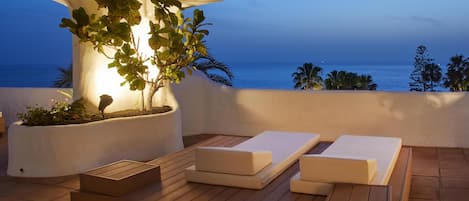 A terrace with wooden lounge chairs and a white planter with plants.