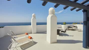 A rooftop terrace with a clear view of the sea, white pillars, and outdoor seating.