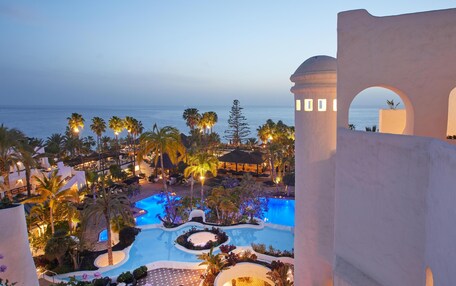 A resort pool area with multiple pools, palm trees, and a view of the ocean at dusk.