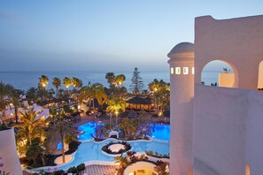 A resort pool area with multiple pools, palm trees, and a view of the ocean at dusk. - Hyatt Ziva Jardín Tropical Tenerife (Adeje)