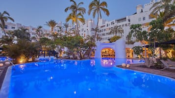 A pool area with palm trees and a building with multiple balconies in the background.
