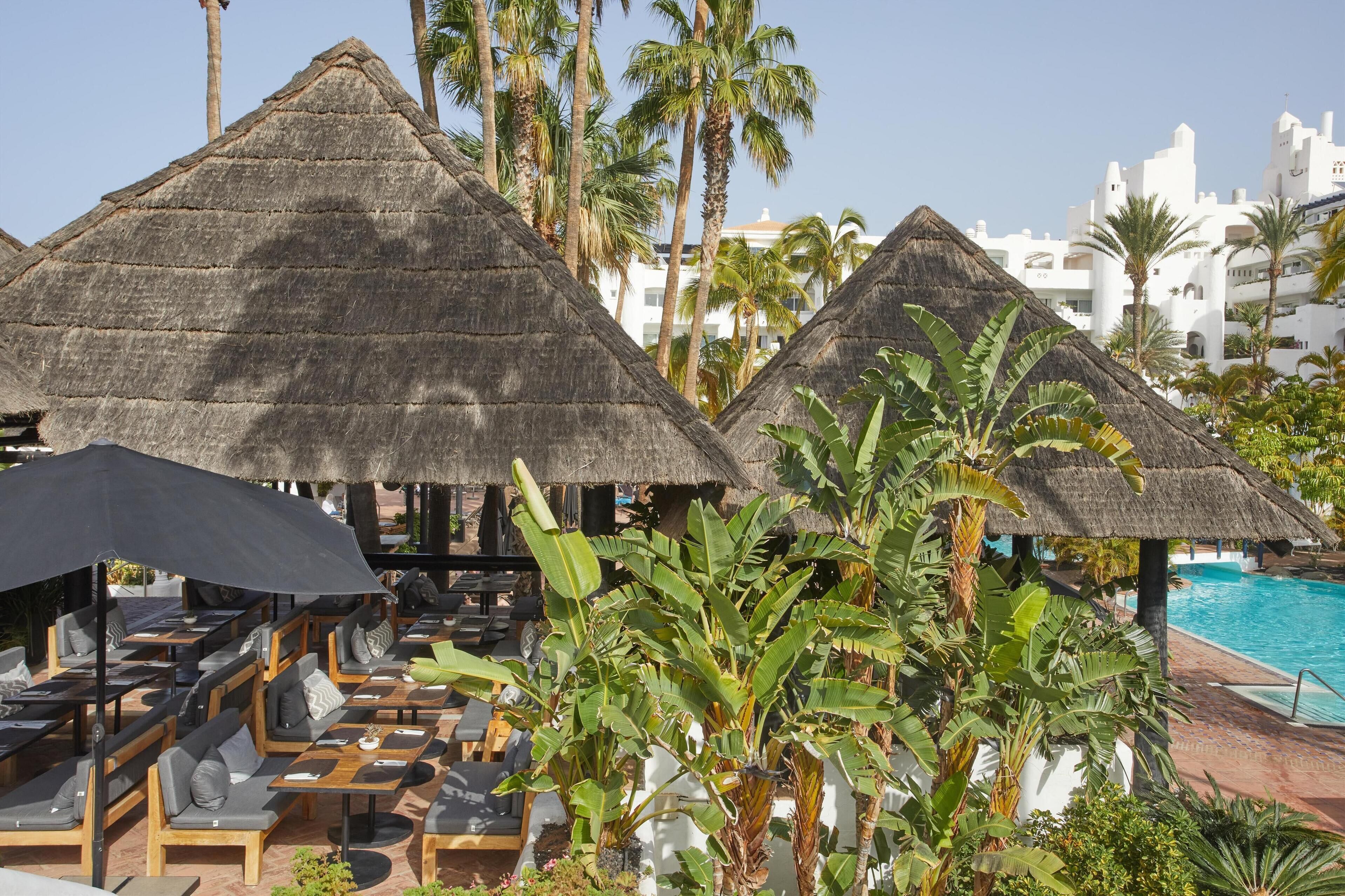 Ett semesterparadis med bungalows med halmtak, solstolar och en pool.