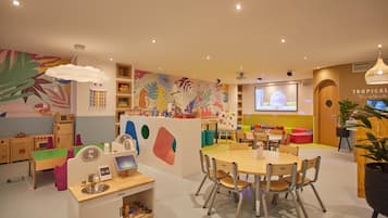 Zona de juegos infantiles con muebles coloridos y una pantalla grande que muestra un personaje animado.