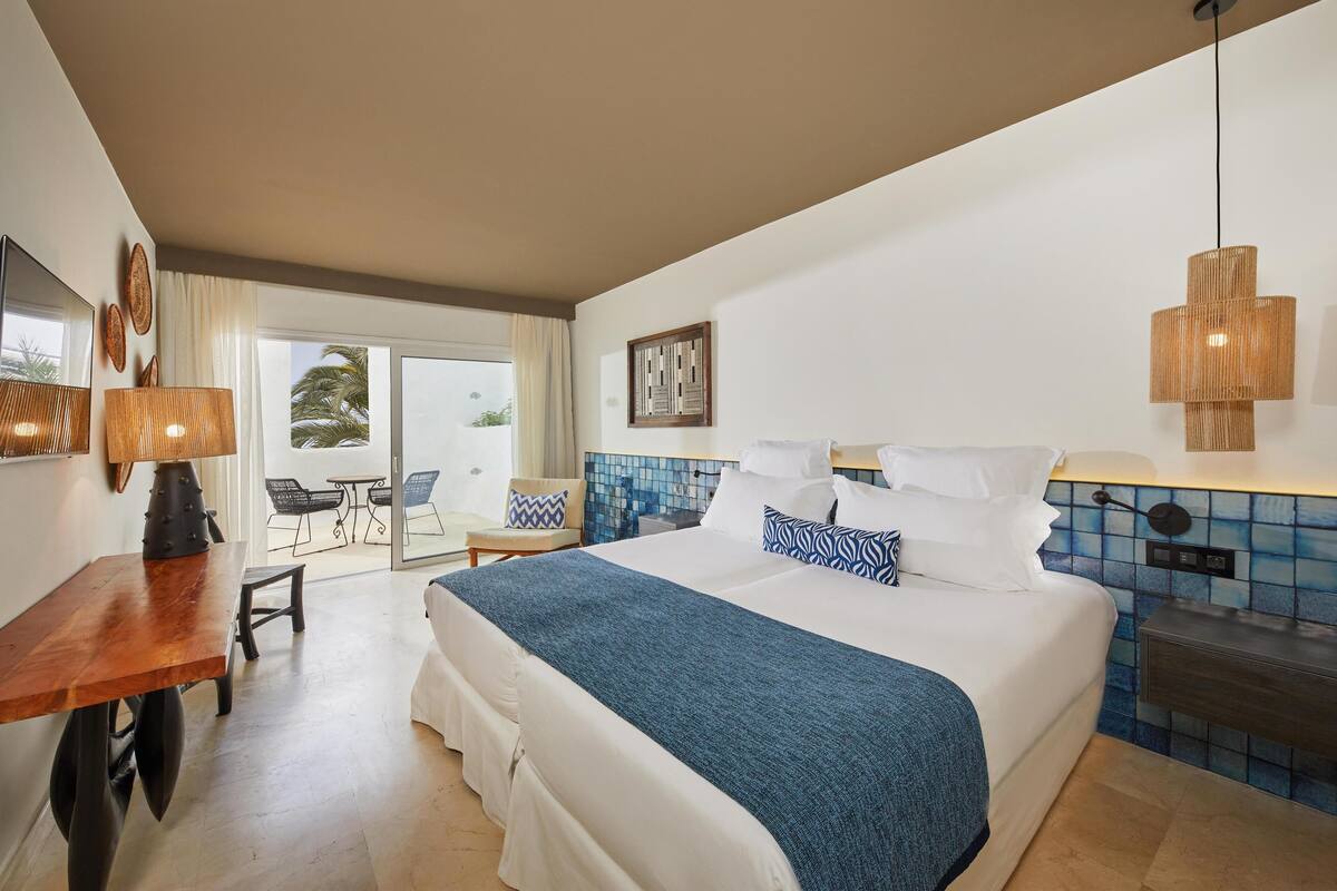 A hotel room with a large bed, a desk, a chair, and a view of the outdoors.