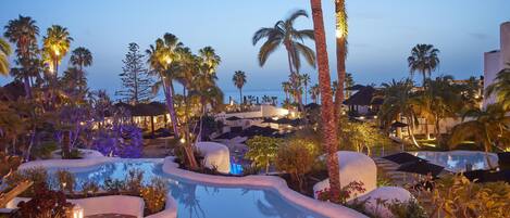 A resort pool area with palm trees, a clear sky, and a well-lit pool.