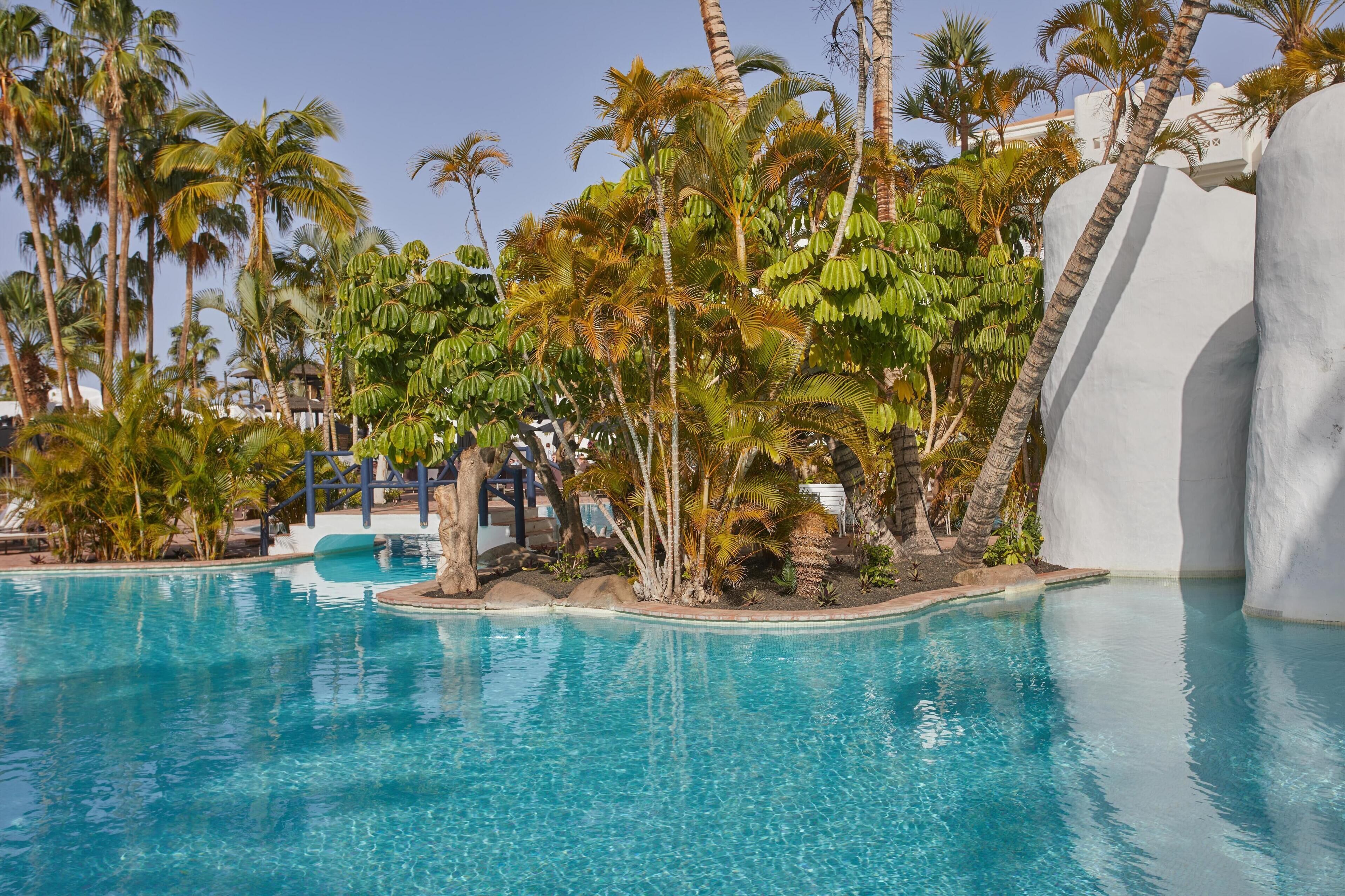 Une piscine entourée de palmiers et un bâtiment blanc.