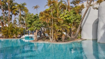 A swimming pool surrounded by palm trees and a white building.