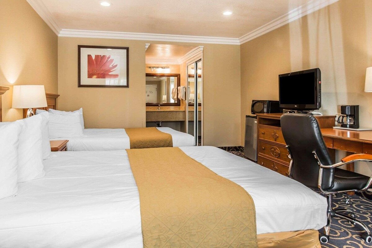 A hotel room with two beds, a desk, a television, and a coffee maker.