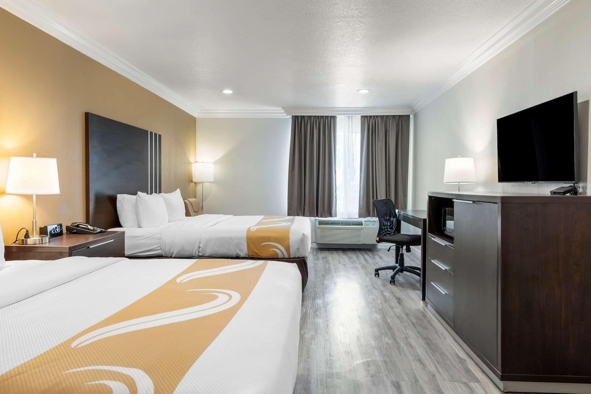 A hotel room with two beds, a desk with a chair, a TV, and a minibar.