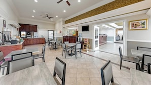 A spacious dining area with multiple tables and chairs, a kitchen in the background, and a ceiling fan.