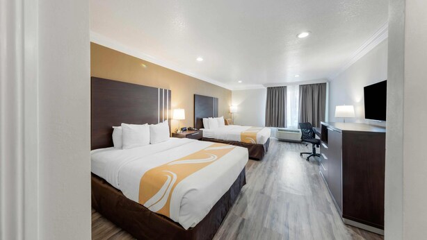 A hotel room with two beds, a desk, a chair, and a television.