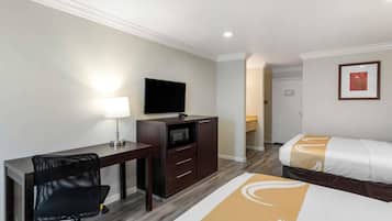 Une chambre d’hôtel équipée d’un bureau, d’une chaise, d’un lit, d’une télévision et d’un four à micro-ondes.