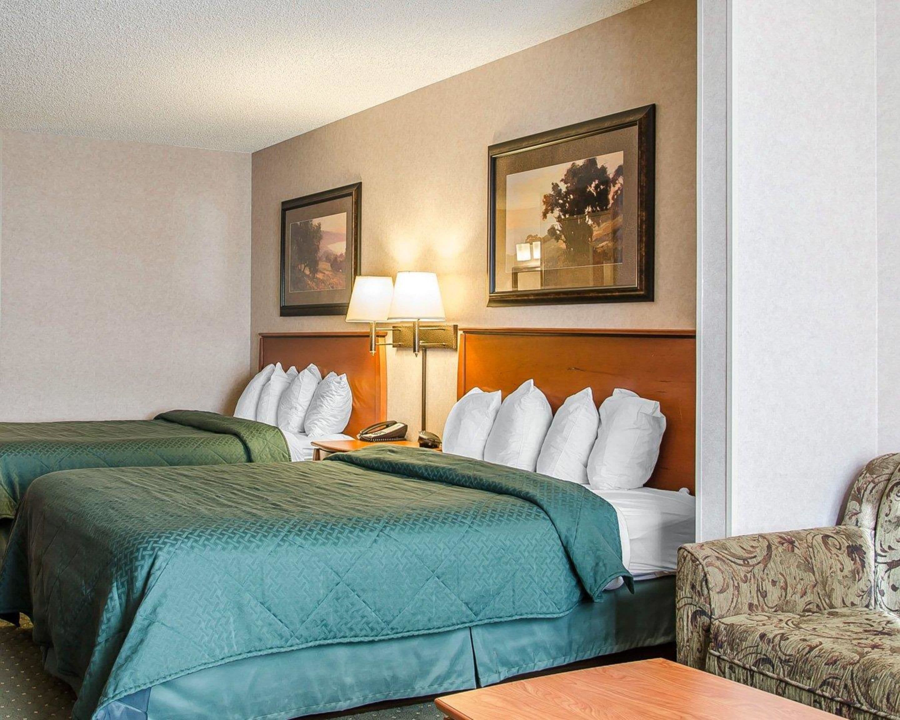 Habitación de hotel con dos camas, una mesita de noche, una lámpara y dos cuadros en la pared.