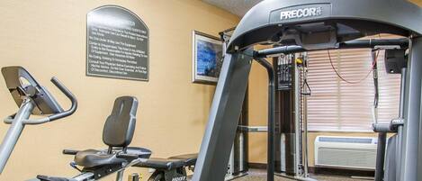 Un gimnasio con cinta de correr, elíptica y máquina de pesas.