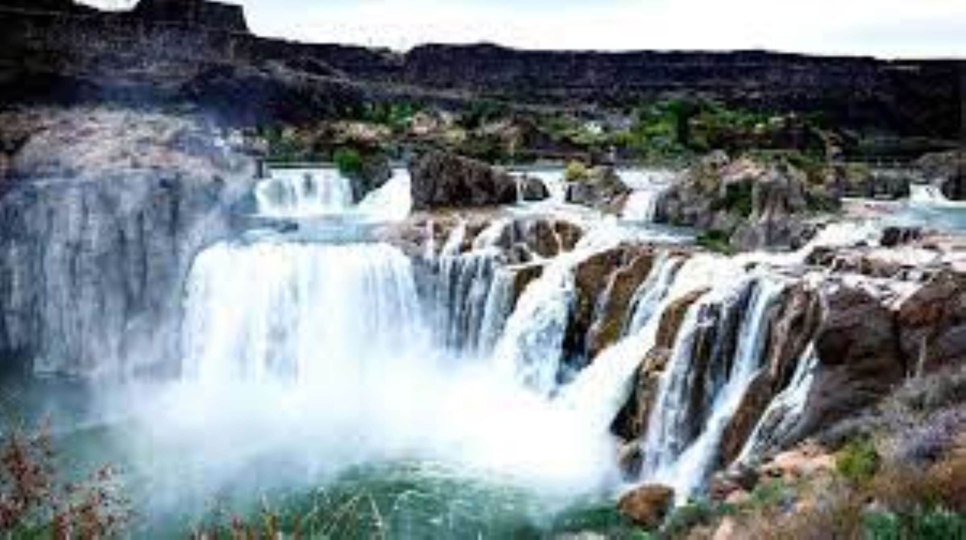 A waterfall with multiple cascades surrounded by rocky terrain and sparse vegetation.