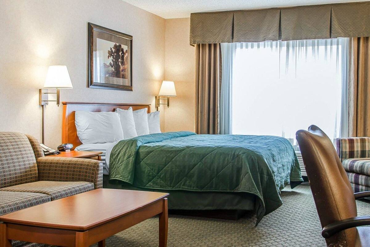 A hotel room with a bed, two bedside tables, a chair, a sofa, a lamp, and a painting on the wall.