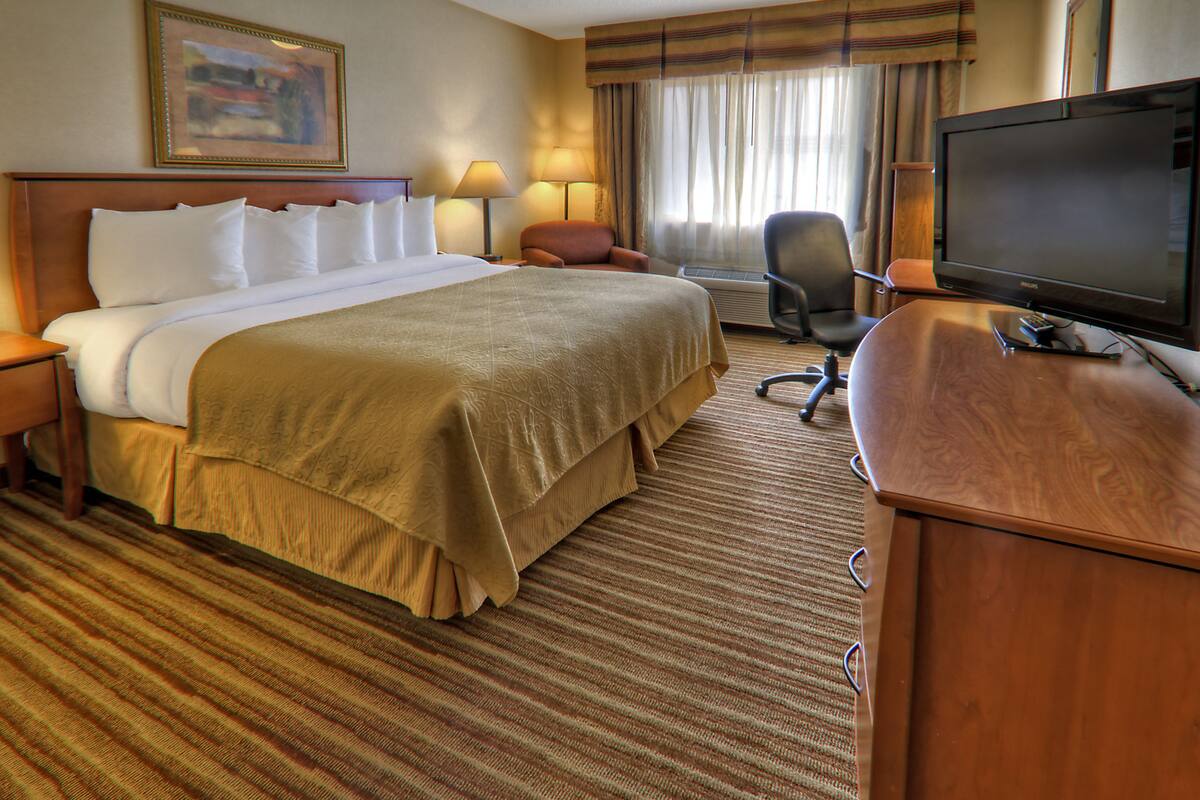 A hotel room with a large bed, a desk with a television, a chair, and a window with curtains.