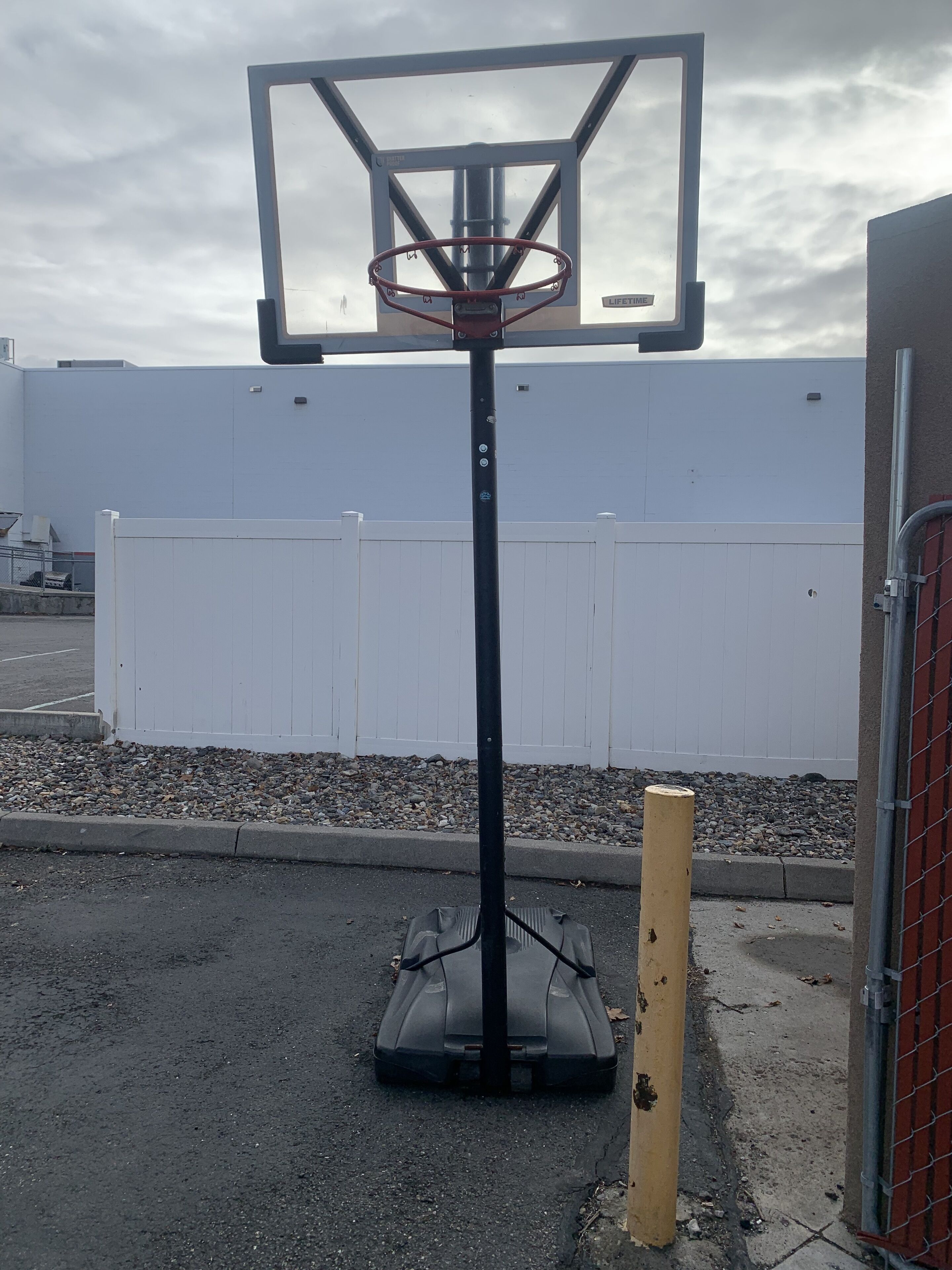 A basketball hoop with a white fence and gravel in the background.