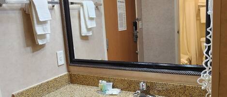 A bathroom with a large mirror, granite countertop, sink, and towel rack.