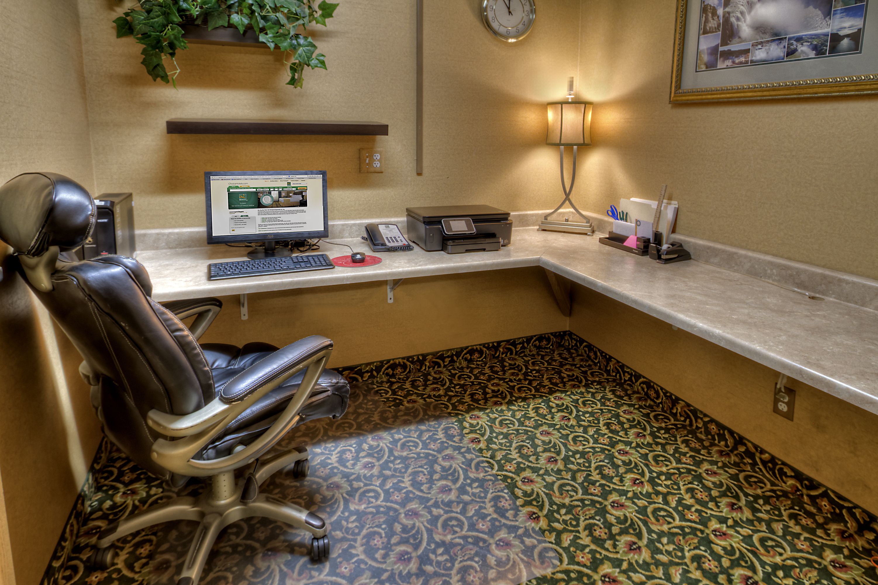 Una oficina de hotel con un escritorio, computadora, teléfono, impresora y una silla.