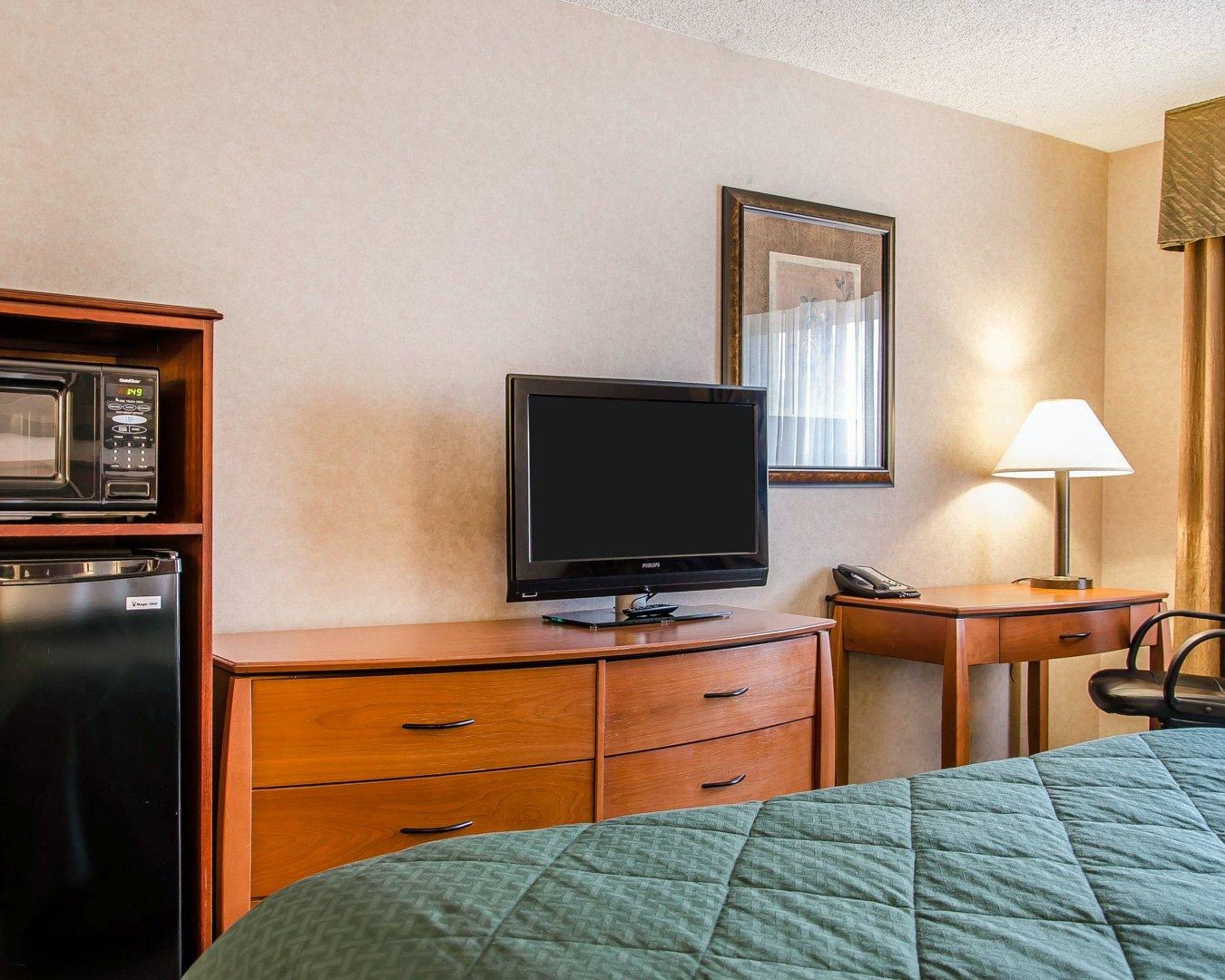 Habitación de hotel con cama, televisión, microondas, refrigerador, escritorio y lámpara.