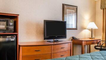 Habitación de hotel con cama, televisión, microondas, refrigerador, escritorio y lámpara.