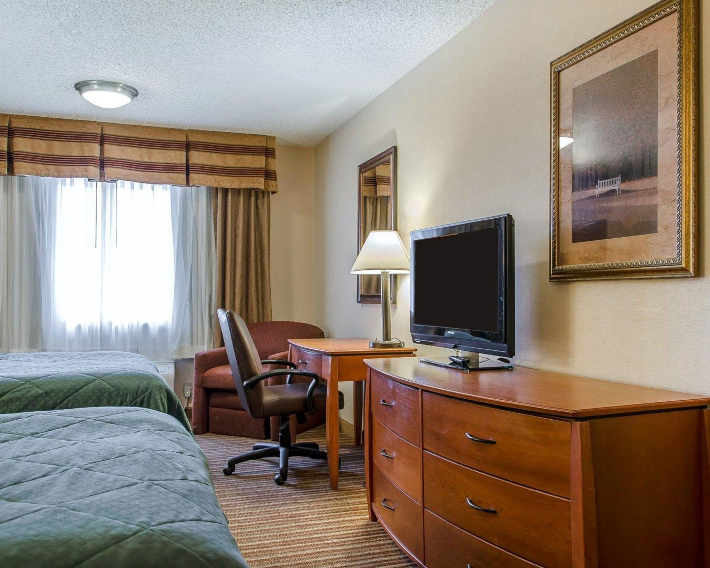 Habitación de hotel con dos camas, un escritorio con computadora, una silla, una lámpara y un cuadro grande enmarcado en la pared.