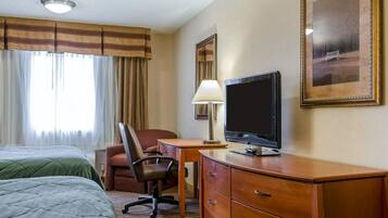 Habitación de hotel con dos camas, un escritorio con computadora, una silla, una lámpara y un cuadro grande enmarcado en la pared.