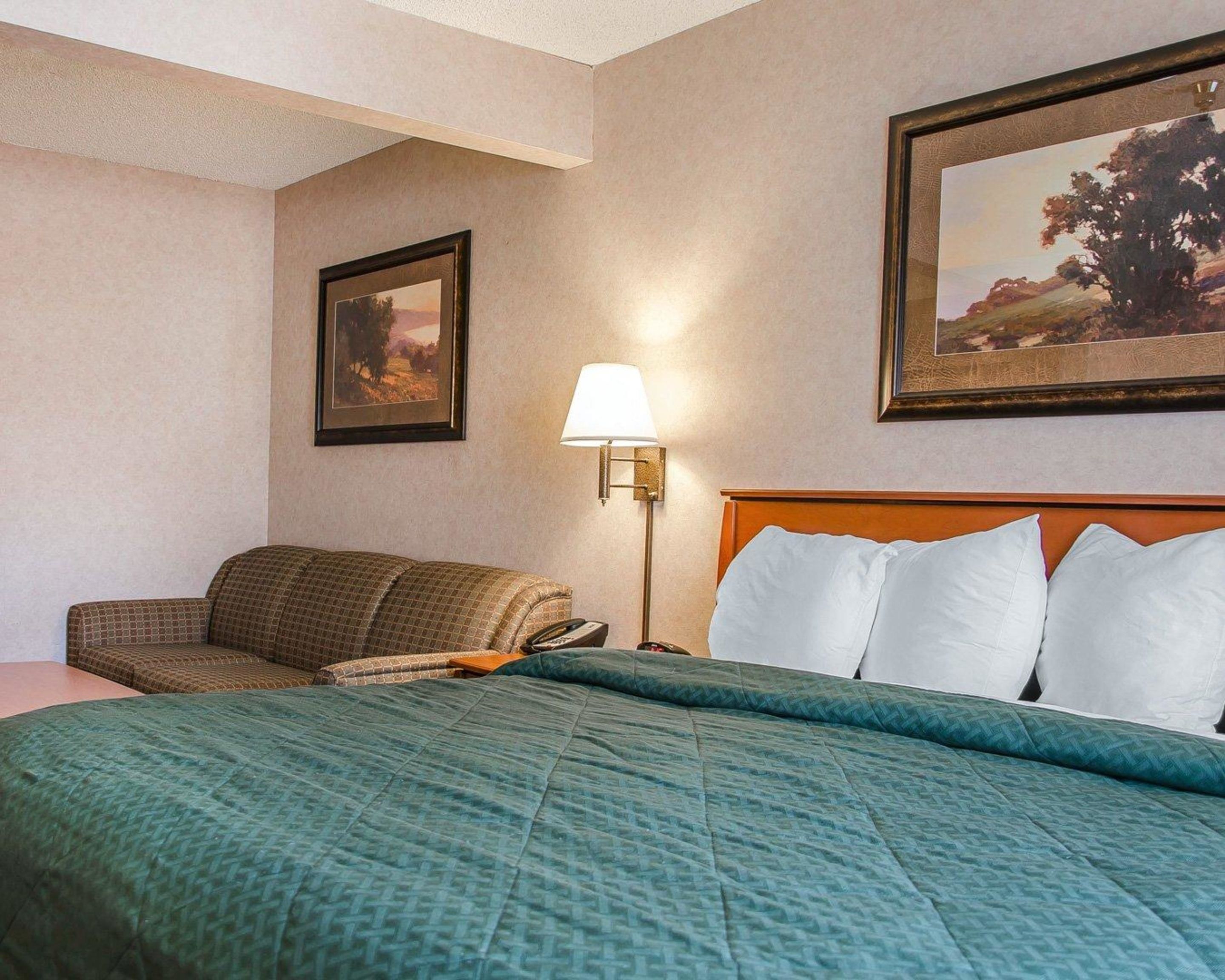 Een hotelkamer met een bed, een bank, een lamp en twee foto's in lijsten aan de muur.