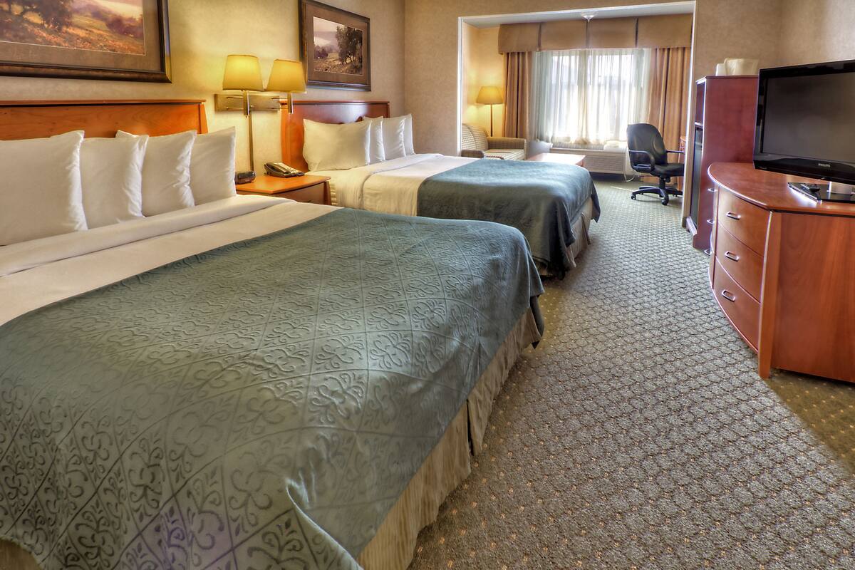 A hotel room with two beds, a desk with a television, a chair, and a lamp.