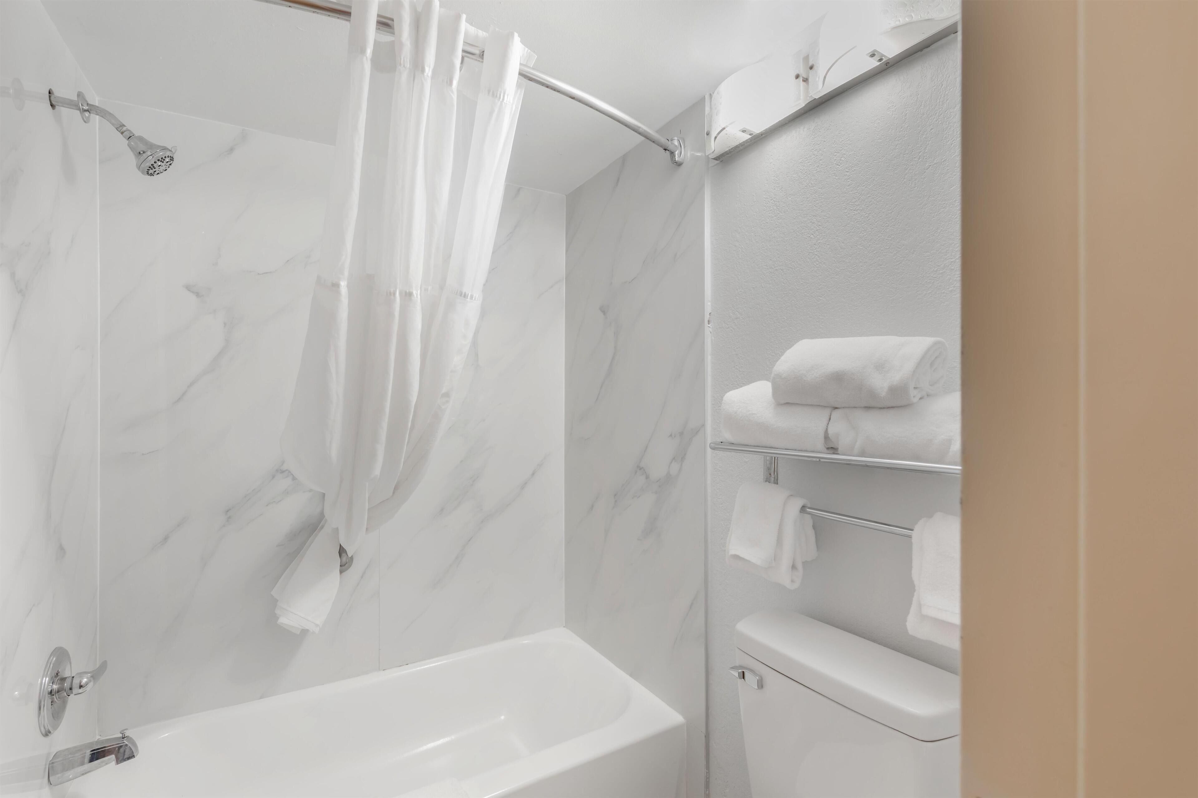 A bathroom with a bathtub, a shower with a curtain, and a towel rack with towels.