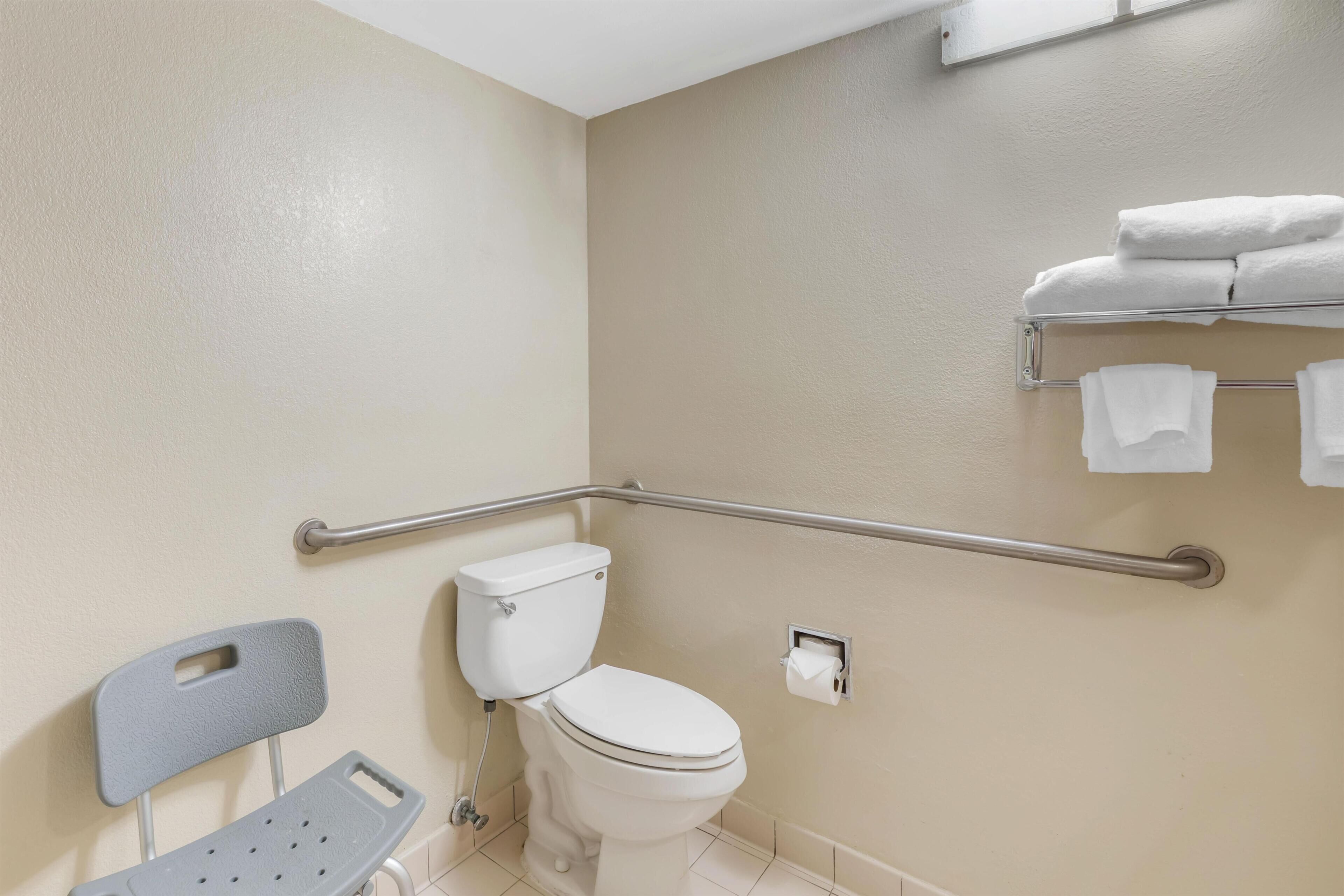 Ein Badezimmer mit Toilette, einer Haltestange, einem Stuhl und einem Handtuchhalter.