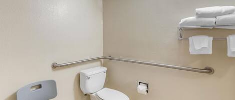 Une salle de bain équipée de toilettes, d’une barre d’appui, d’une chaise et d’un porte-serviettes.