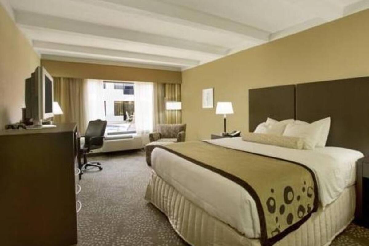 Une chambre d’hôtel avec un grand lit, un bureau, une chaise et une fenêtre avec des rideaux.