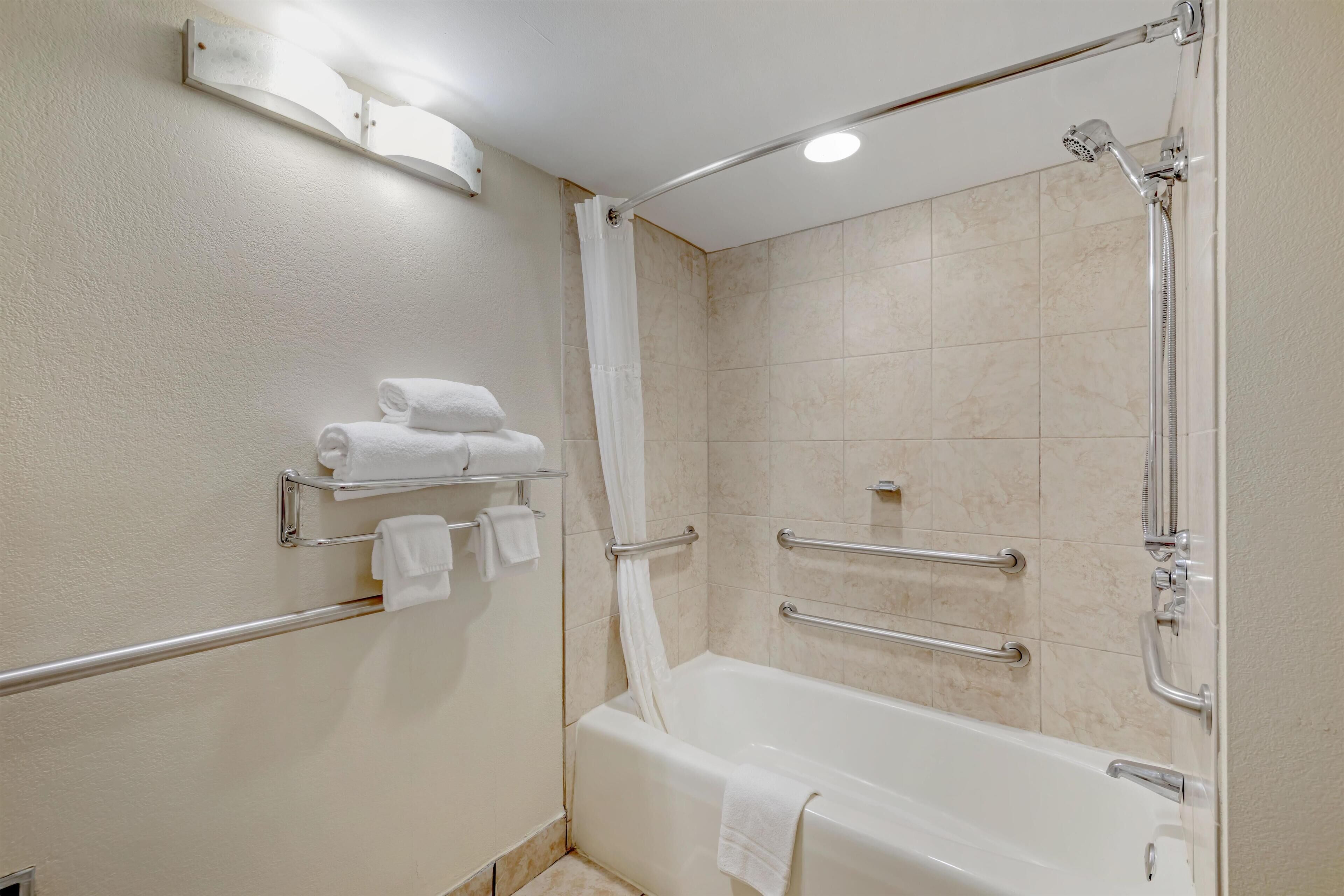 A modern bathroom with a bathtub, shower, and handrails.
