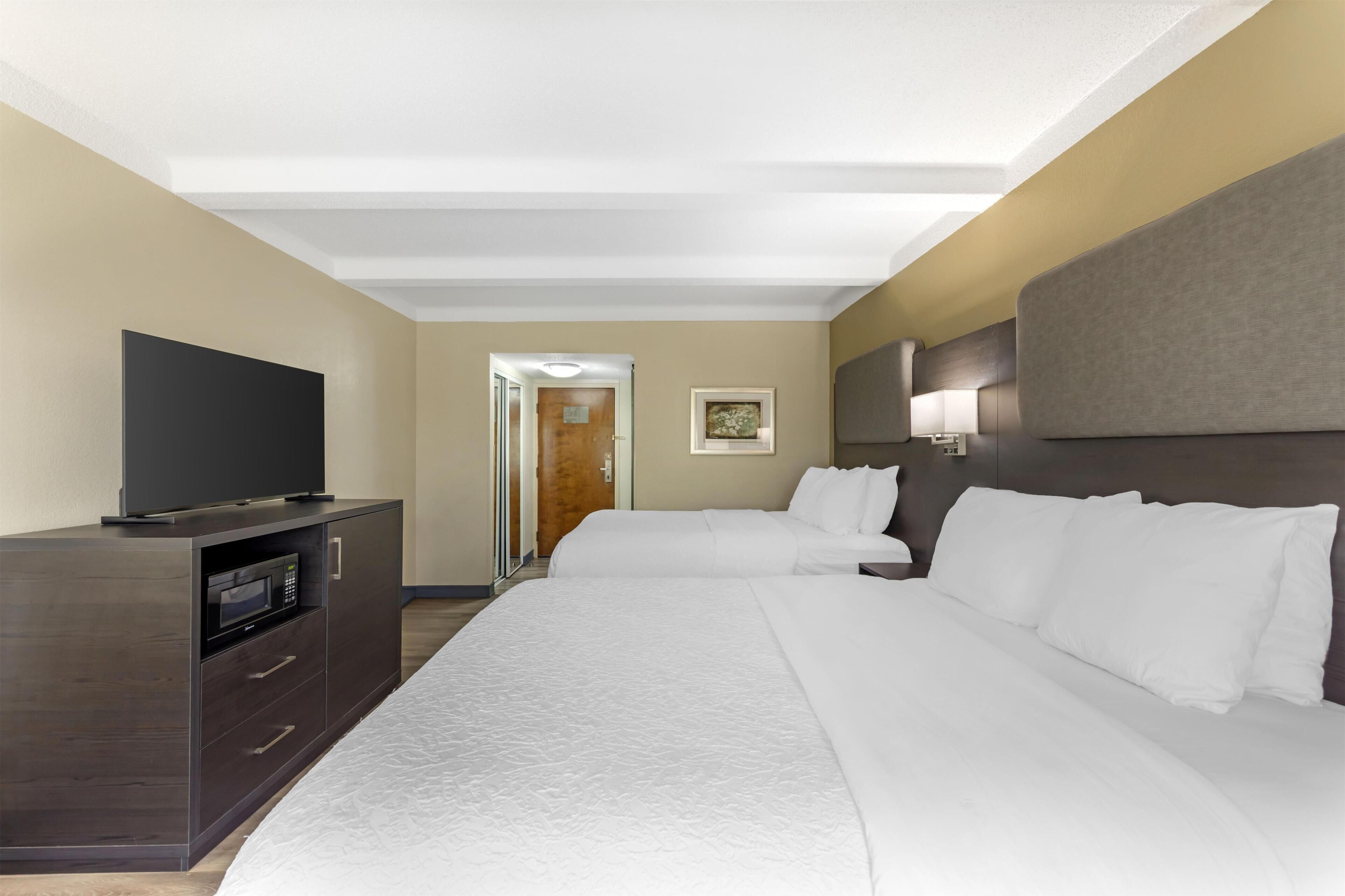 Une chambre d’hôtel avec deux lits, une télévision, un minibar et une porte donnant sur un couloir.