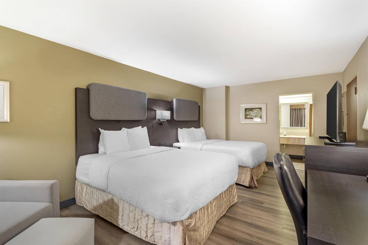 Une chambre d’hôtel avec deux lits, un bureau, une chaise, une télévision et un tableau encadré au mur.