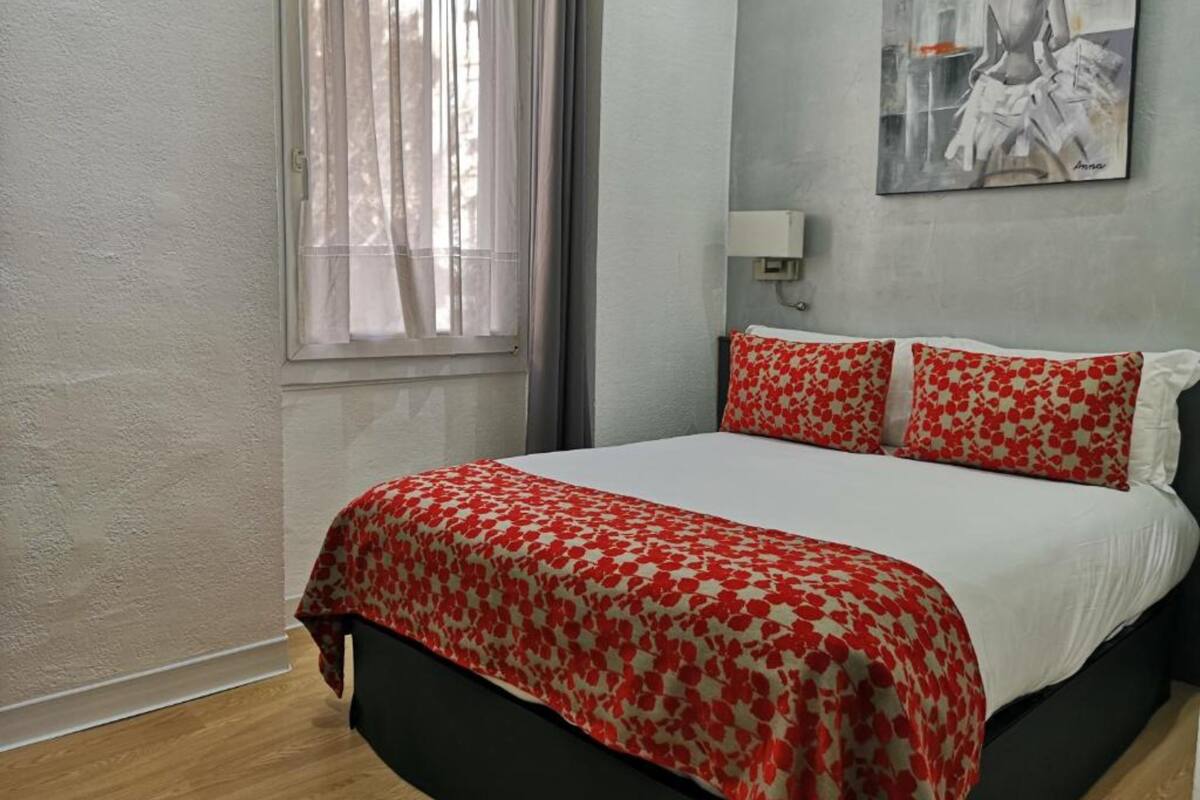 Een slaapkamer met een bed, een raam met gordijnen, een schilderij aan de muur en een bedlampje.
