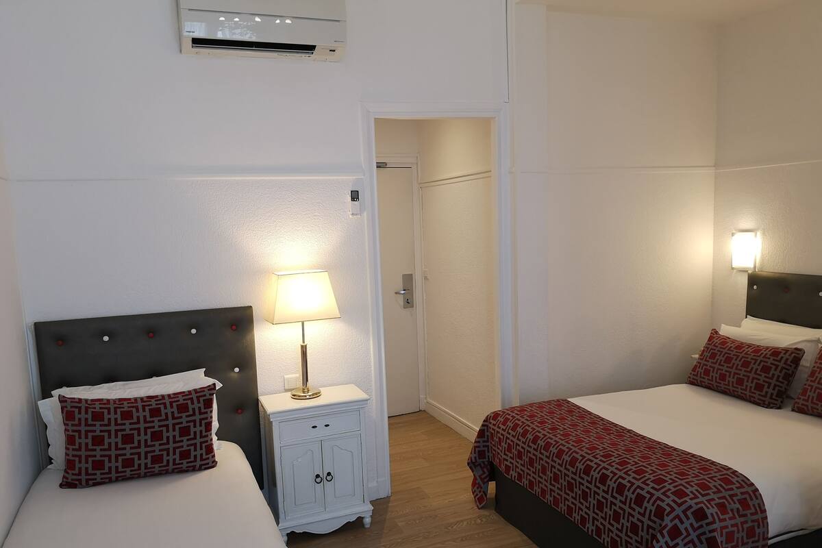 Een hotelkamer met twee bedden, een nachtkastje met een lamp, een garderobe en een airconditioning.