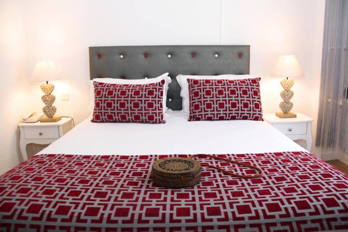 Een opgemaakt bed met een beddengoed met een patroon, twee kussens met een geometrisch ontwerp, en een nachtlampje aan beide zijden.