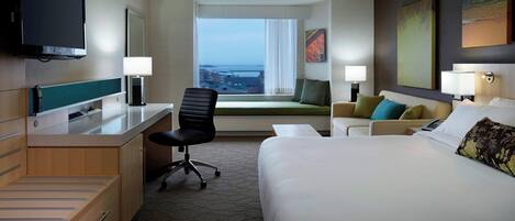 Habitación de hotel con cama, escritorio, silla, televisor y un amplio ventanal con vistas.