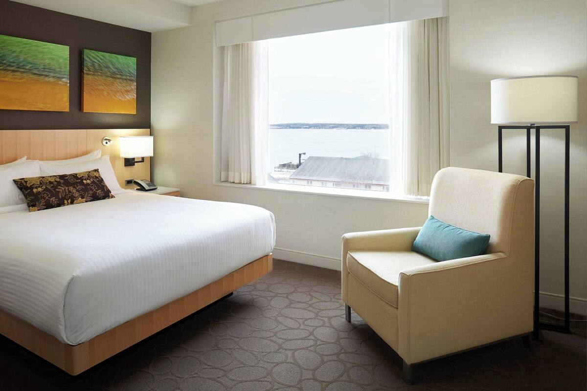 A hotel room with a large bed, a chair, a lamp, and a view of the water.