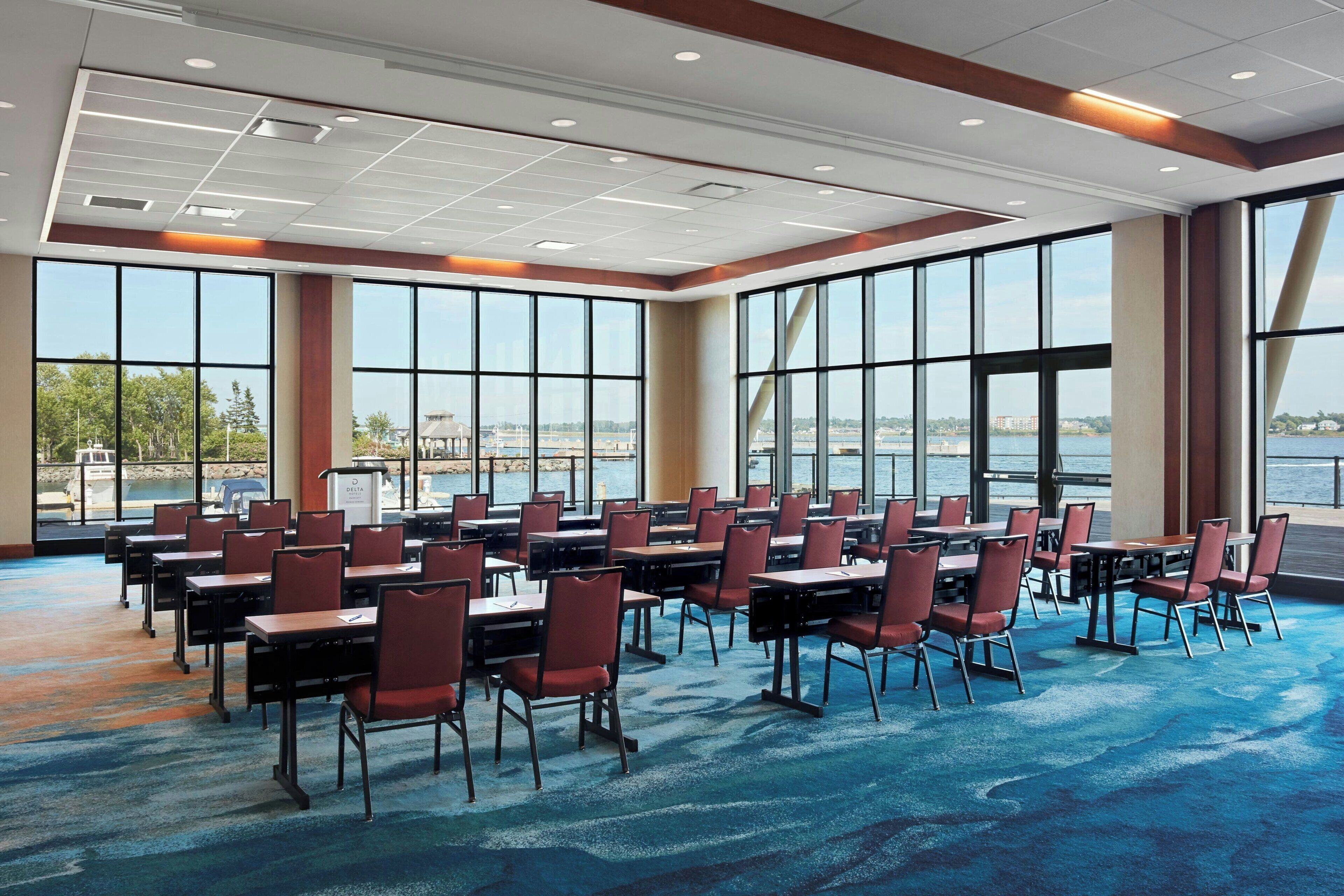 A conference room with large windows, a blue carpet, and rows of tables and chairs.