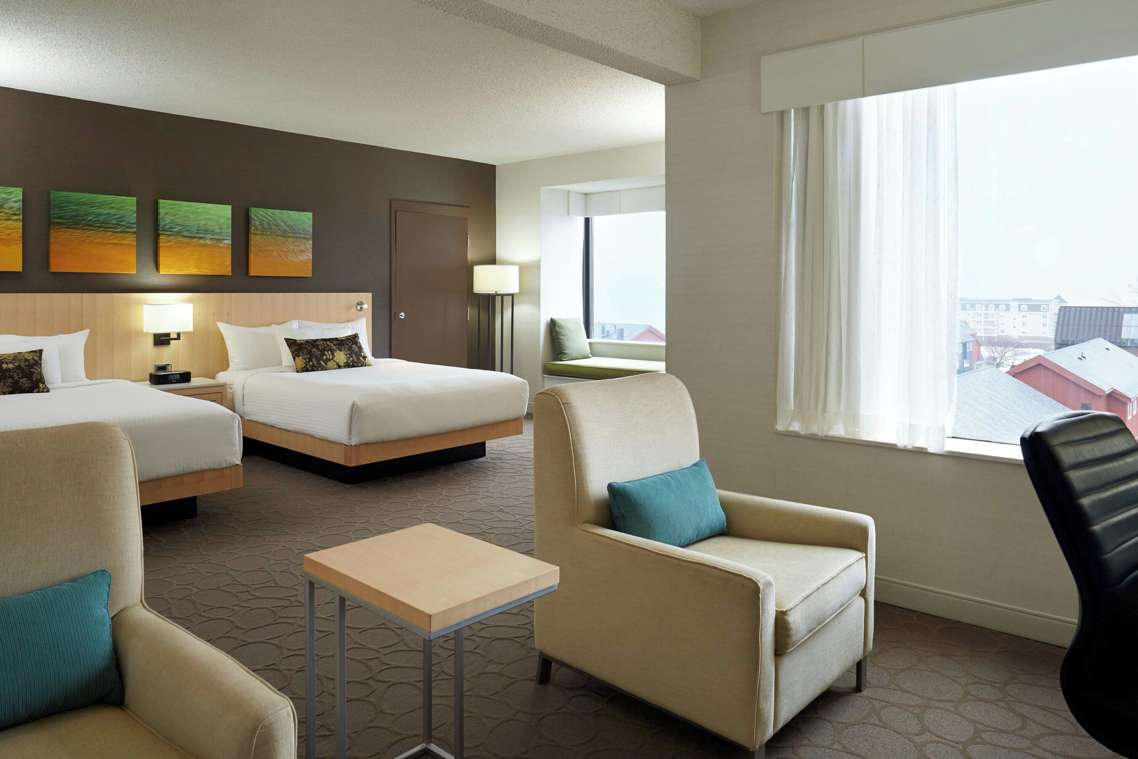 A hotel room with two beds, a sofa, a chair, a small table, and a window with a view.
