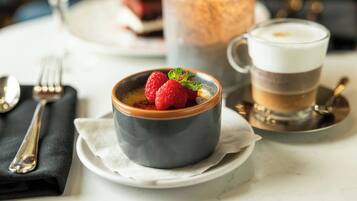 Un tazón de postre con frambuesas y menta sobre un plato blanco, una vela y una taza de café en una mesa.