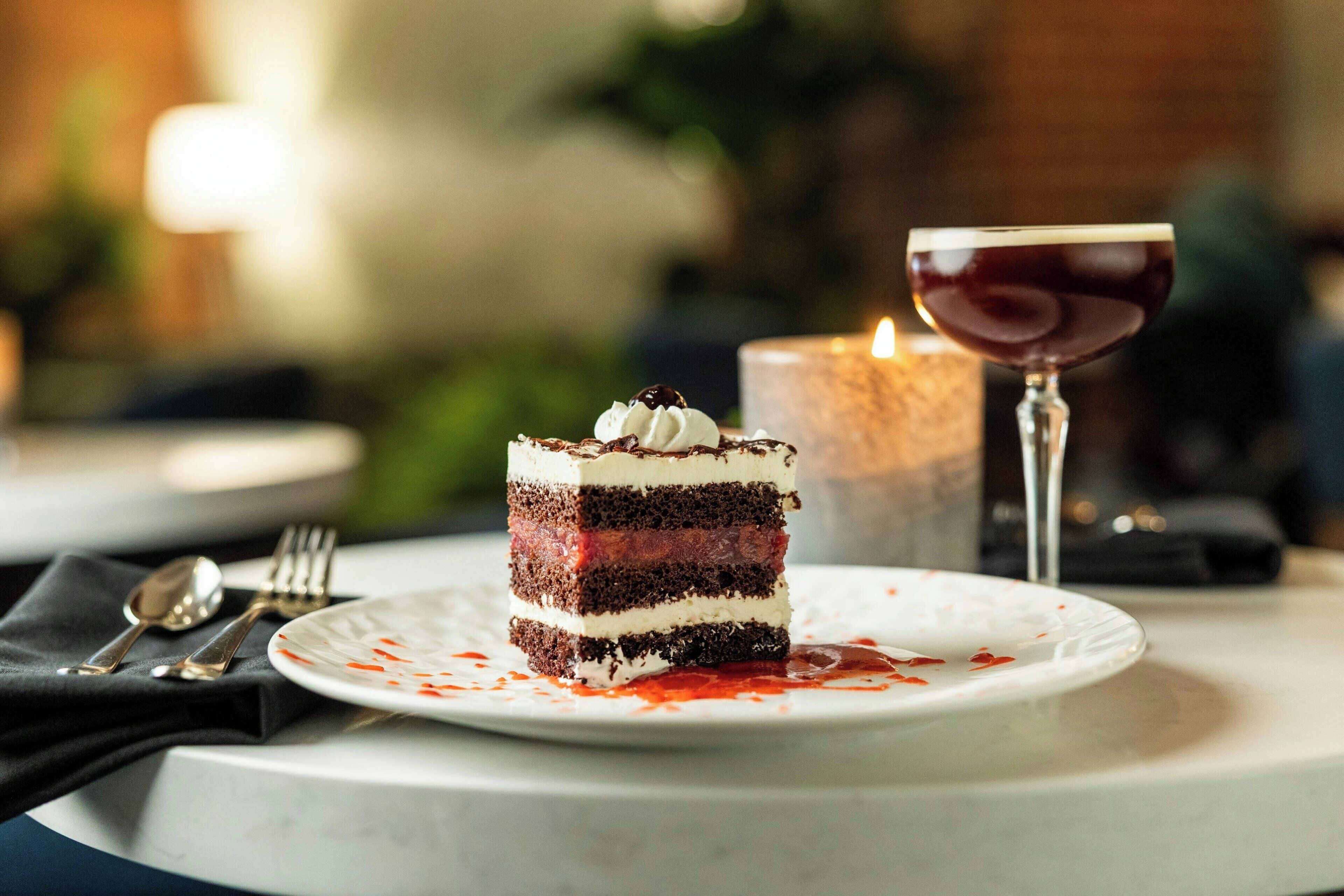 A slice of layered cake on a white plate with a glass of red wine beside it.