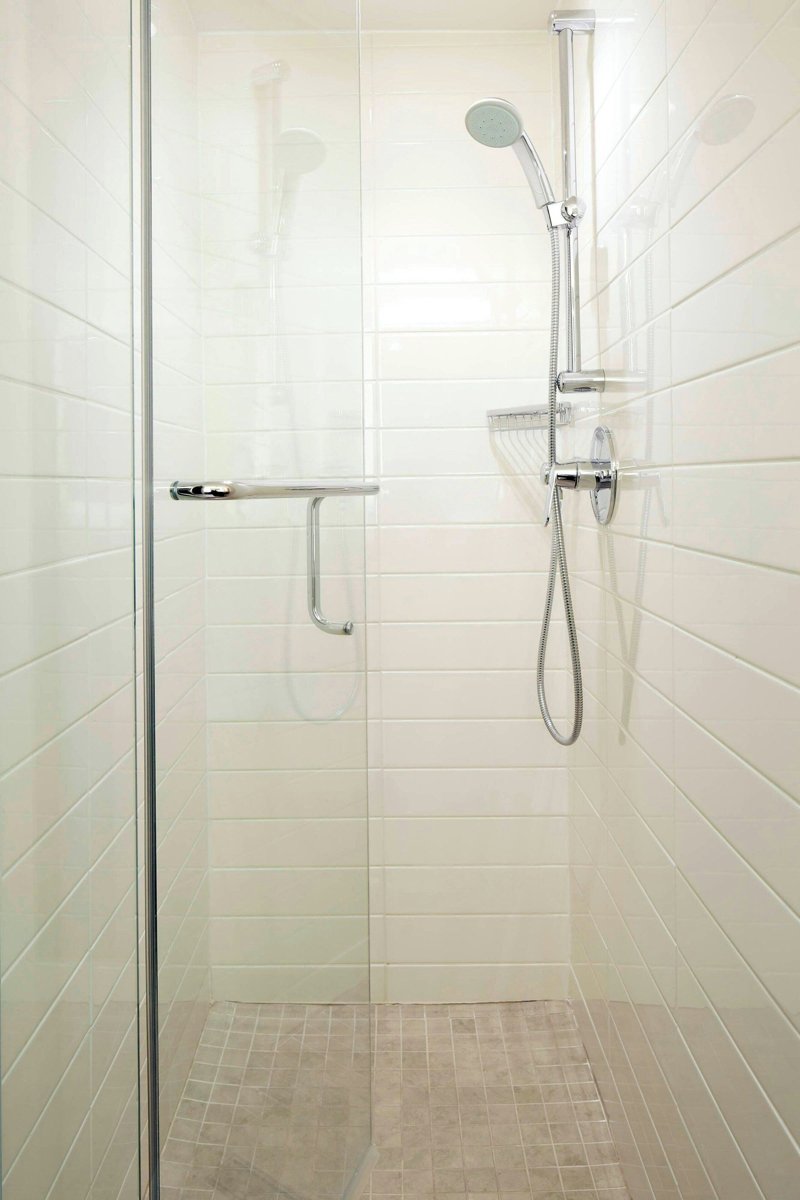 Eine moderne Dusche mit Handbrause und fest installierter Duschbrause, einer Glasduschwand und einer Metall-Haltestange.